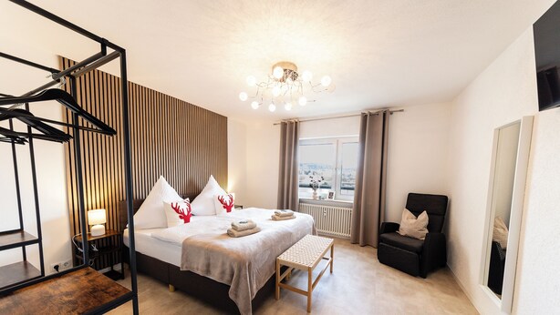A modern bedroom with a bed, bedside tables, a bench, a chair, and a view of the outdoors. - Holiday Apartment 120 m² Penthouse – Europa-Park – Strasbourg – Colmar (Lahr/Schwarzwald)