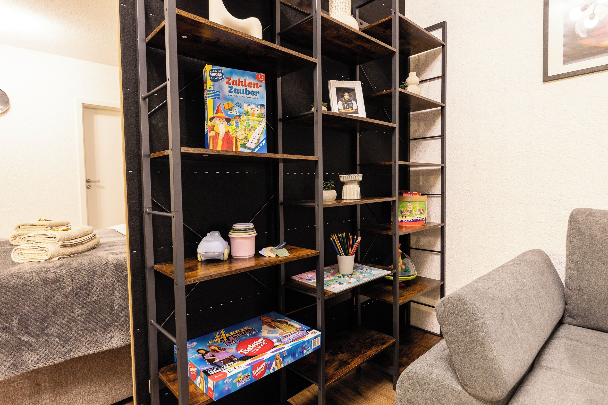 Een kamer met een boekenkast vol gezelschapsspellen, een ingelijste foto en een kleine plant in pot.