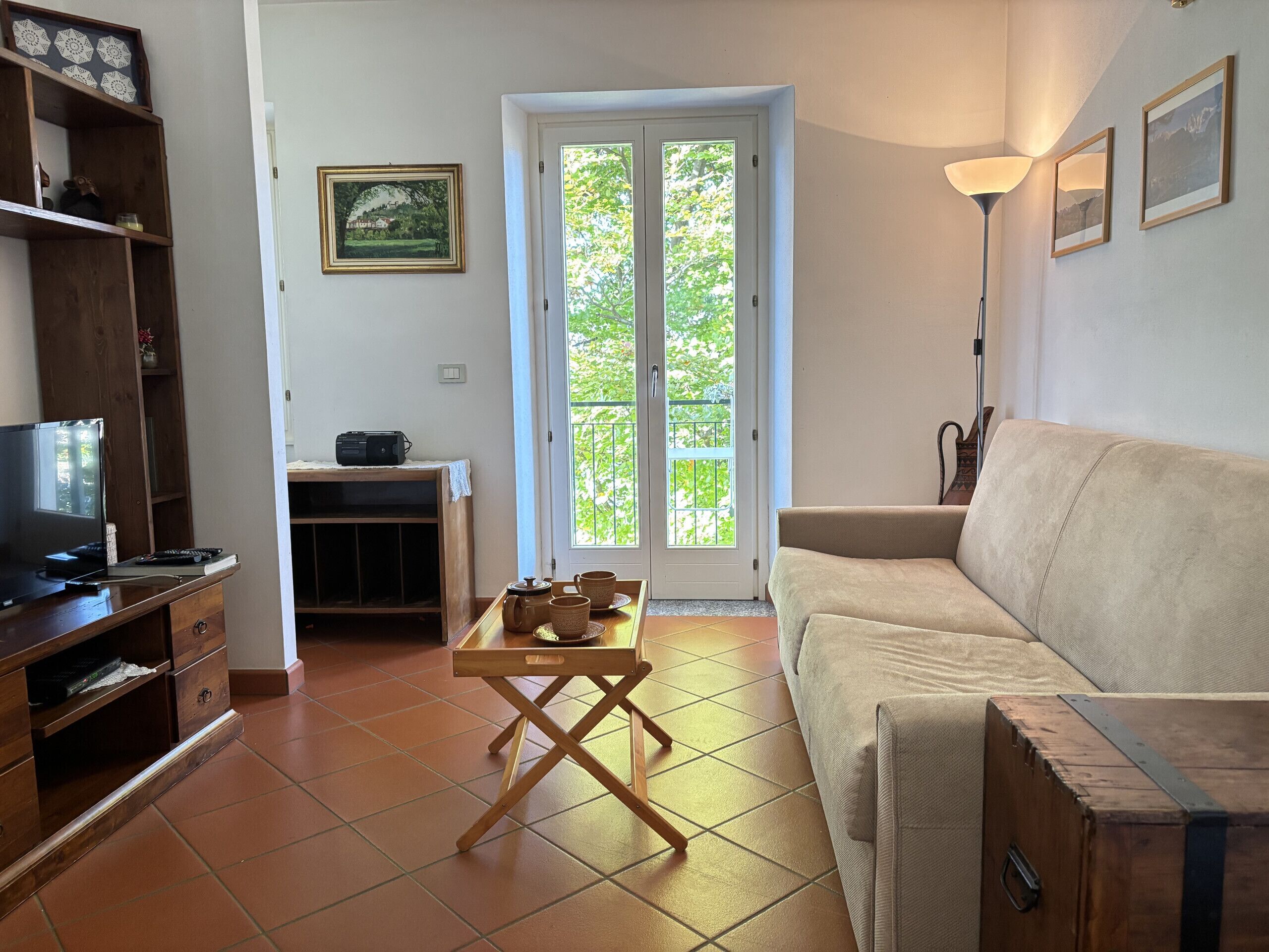 A living room with a sofa, a television, a wooden cabinet, a table with cups, and a balcony door.