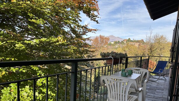 A balcony with a table and chairs, a potted plant, and a view of a mountain and buildings. - Esther 2 apartment with balcony in Luino (Luino)