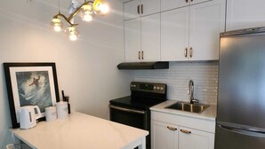 Een moderne keuken met witte kasten, een roestvrijstalen koelkast, een zwart fornuis en een witte eettafel met stoelen.