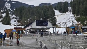 Een skigondelstation met een bus, besneeuwde bergen en een bebost gebied.