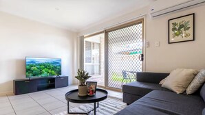 A modern living room with a flat-screen TV, a sofa, a coffee table with a plant, and a sliding glass door leading to a balcony.