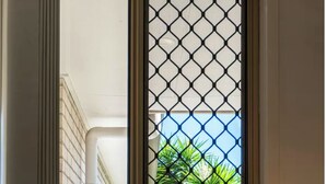 A hotel room with a view of a garden through a window with a metal grid.