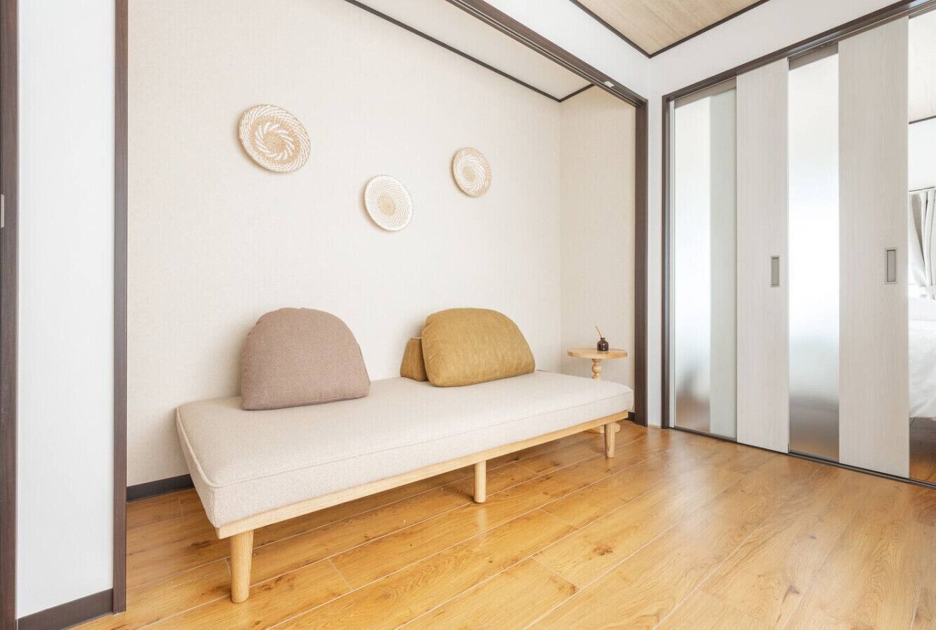 Ein schlichter Raum mit Holzboden, einem weißen Sofa mit zwei Kissen und einem kleinen runden Tisch.