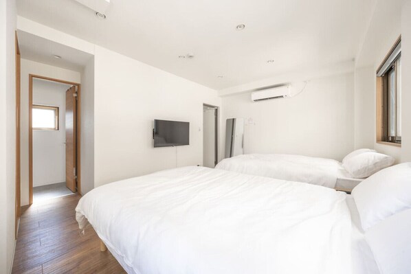 A modern bedroom with two beds, a flat-screen TV mounted on the wall, and an air conditioning unit.