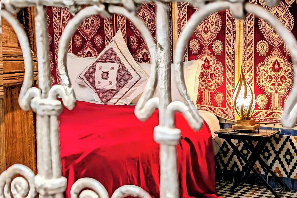 A bed with a red cover, a patterned wall, and a decorative metal frame.