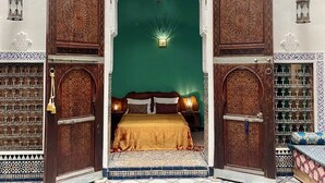 Une pièce avec un mur vert, un lit recouvert d’une couvre-lit dorée, ainsi que des portes et des murs en bois richement décorés.