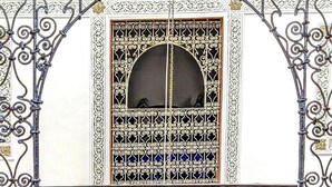 Une porte en fer forgé décorative, ornée de motifs complexes et dotée d’une fenêtre en arc de cercle au centre.