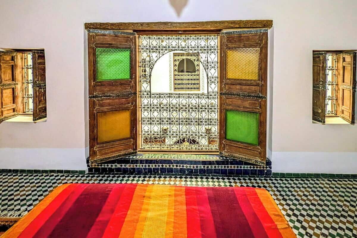 A room with a checkered floor, a colorful striped rug, and a decorative wooden screen with green panels.