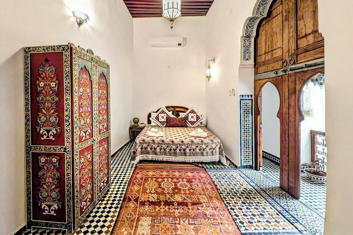 A traditional room with a bed, patterned rugs, and a wooden door.