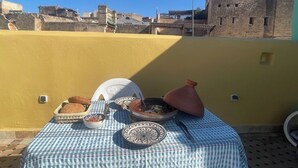 Une table dressée avec de la nourriture et un pot en argile traditionnel, le tout installé sur une terrasse en toit offrant une vue sur la ville.