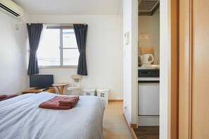 A hotel room with a bed, a TV, a small table, a chair, a desk, a kitchenette, and a window with curtains. - Shinjuku 202 for 2 peoples, private toilet + small kitchen (中野區)