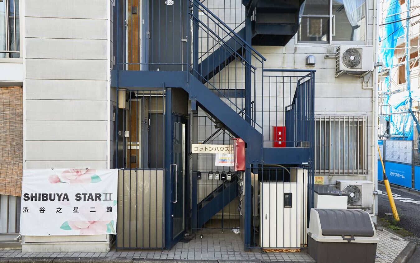 A building entrance with a blue staircase, a sign reading "SHIBUYA STAR III," and a trash bin.