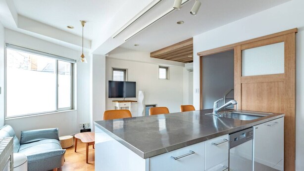Une cuisine moderne dotée d’un îlot central, d’un lave-vaisselle encastré et d’un coin repas avec des chaises orange.