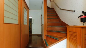 A wooden staircase with a handrail, a carpeted landing, and a door leading to a room with a patterned wall. - House Near Shinjuku Central Park! (Shinjuku-ku)