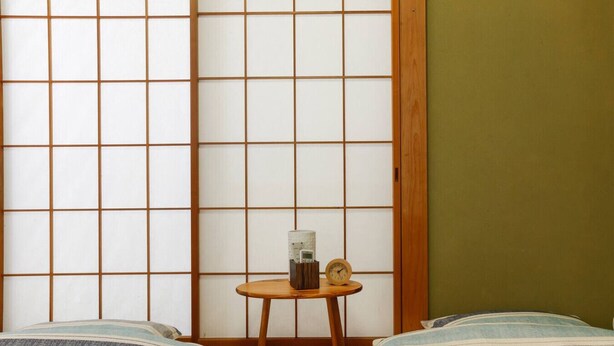 A traditional Japanese room with tatami flooring, a shoji screen, and a small wooden table with a clock and a container. - House Near Shinjuku Central Park! (Shinjuku-ku)