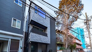 Un edificio residencial moderno de dos pisos, con puerta de garaje, un pequeño porche delantero y un cuadro eléctrico visible.