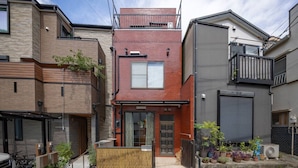 A modern residential building with a red brick facade, a wooden front porch, and a grey garage door. - Kiki`s Delivery Service | Within walking distance of Ikebukuro | A Tokyo home immersed in Studio Ghibli fairy tales (Toshima City)