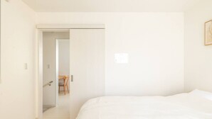 A bedroom with a bed, a door leading to a bathroom, and a chair in the adjacent room. - Near Shinjuku 3 stops (Suginami City)