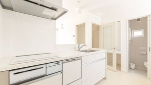 A modern kitchen with white cabinetry, a stainless steel range hood, and a built-in dishwasher. - Near Shinjuku 3 stops (Suginami City)