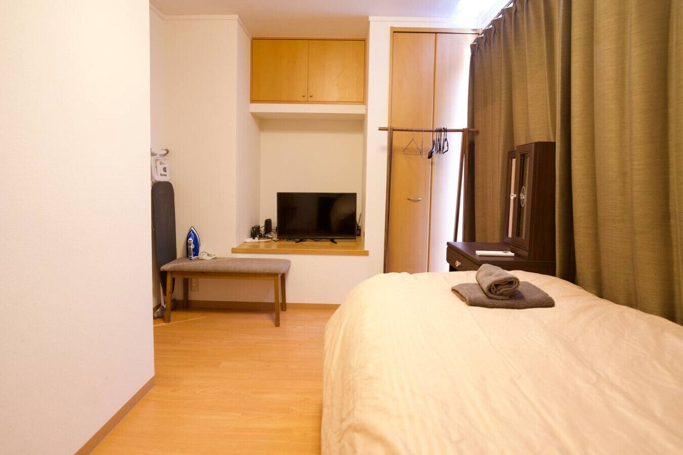 A hotel room with a bed, a bench, a TV, a wooden cabinet, and a window with curtains.