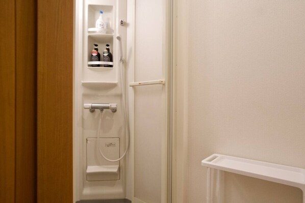 A bathroom with a shower, a toilet, and a shelf with toiletries. - Iriya no Hoshi, up to 9 people, Just 2 minutes walk to Iriya station (Taito City)