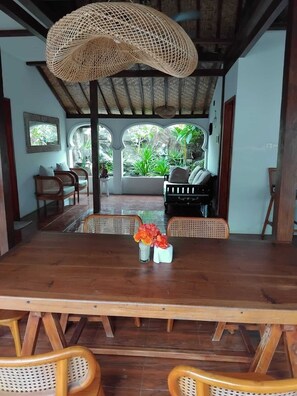 A wooden dining table with two vases of flowers, wicker chairs, and a woven ceiling light fixture. - Ardi Beltza Villa (Gili Air)