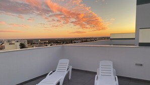 Una terrazza sul tetto con due poltrone bianche e vista sulla città al tramonto.