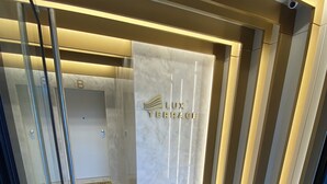 Una veduta interna di una moderna hall d'albergo con una reception in marmo, un ascensore in vetro e un tappetino marrone sul pavimento.