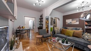 A modern living room with a grey sofa, a glass coffee table, and a dining area with a glass table and chairs. - Alopece City Apartment (Athens)