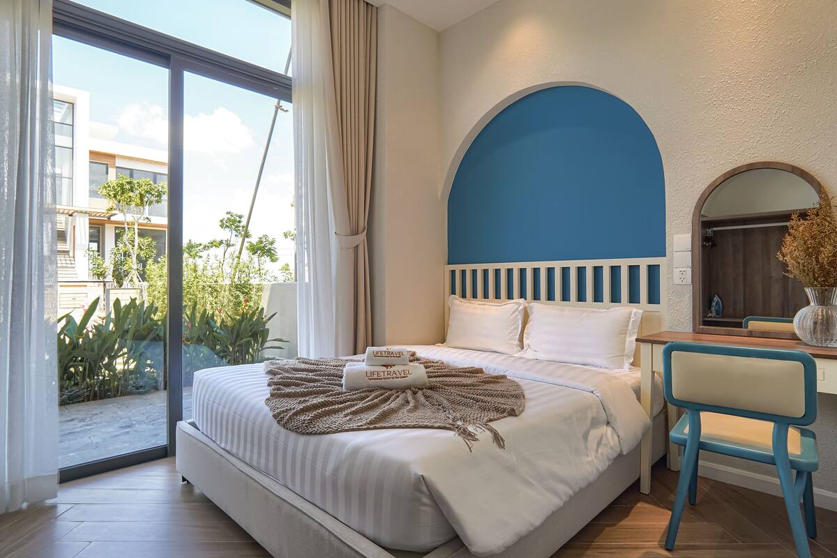 A hotel room with a bed, a desk, a chair, and a view of the outside.
