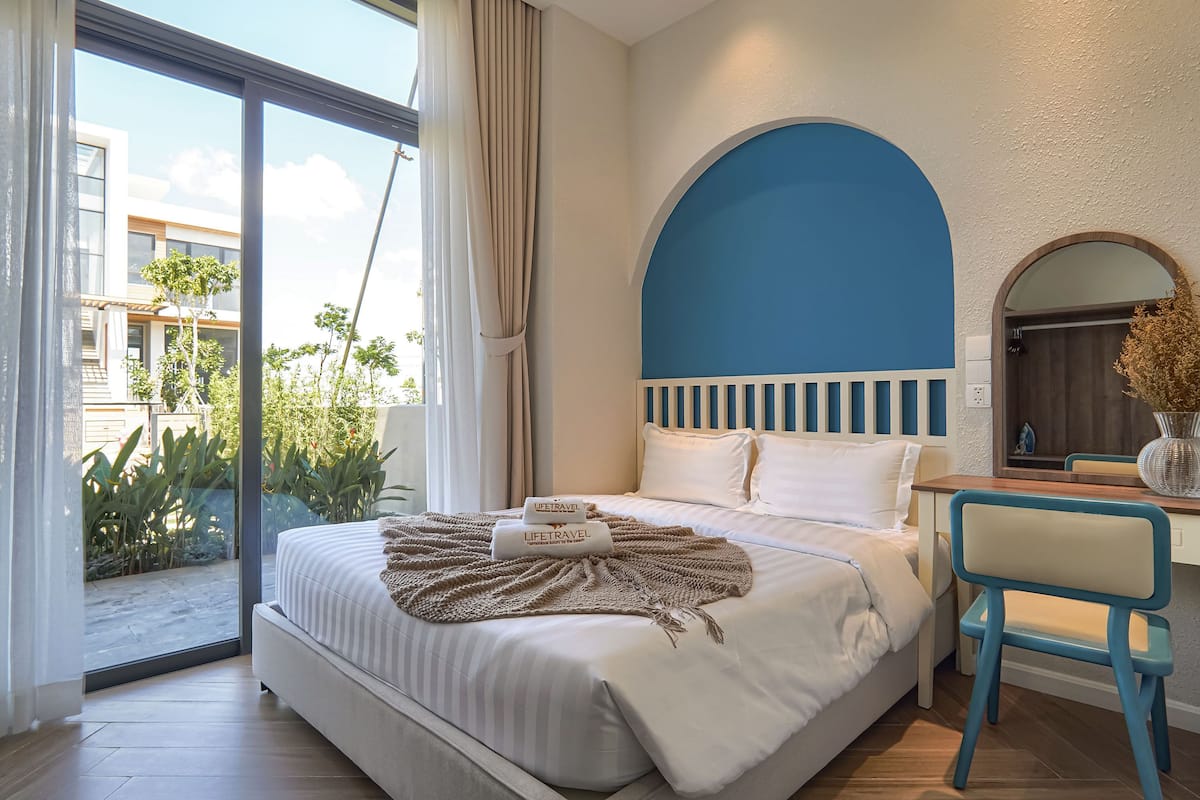 A hotel room with a bed, a desk, a chair, and a view of the outside.