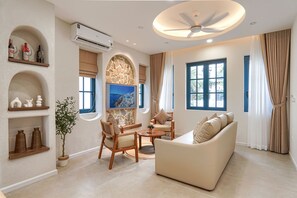 A modern living room with a sofa, chairs, a coffee table, and a TV. There are shelves with decorative items and a potted plant. - Life Travel Villa - Novaworld Phan Thiet (Phan Thiet)