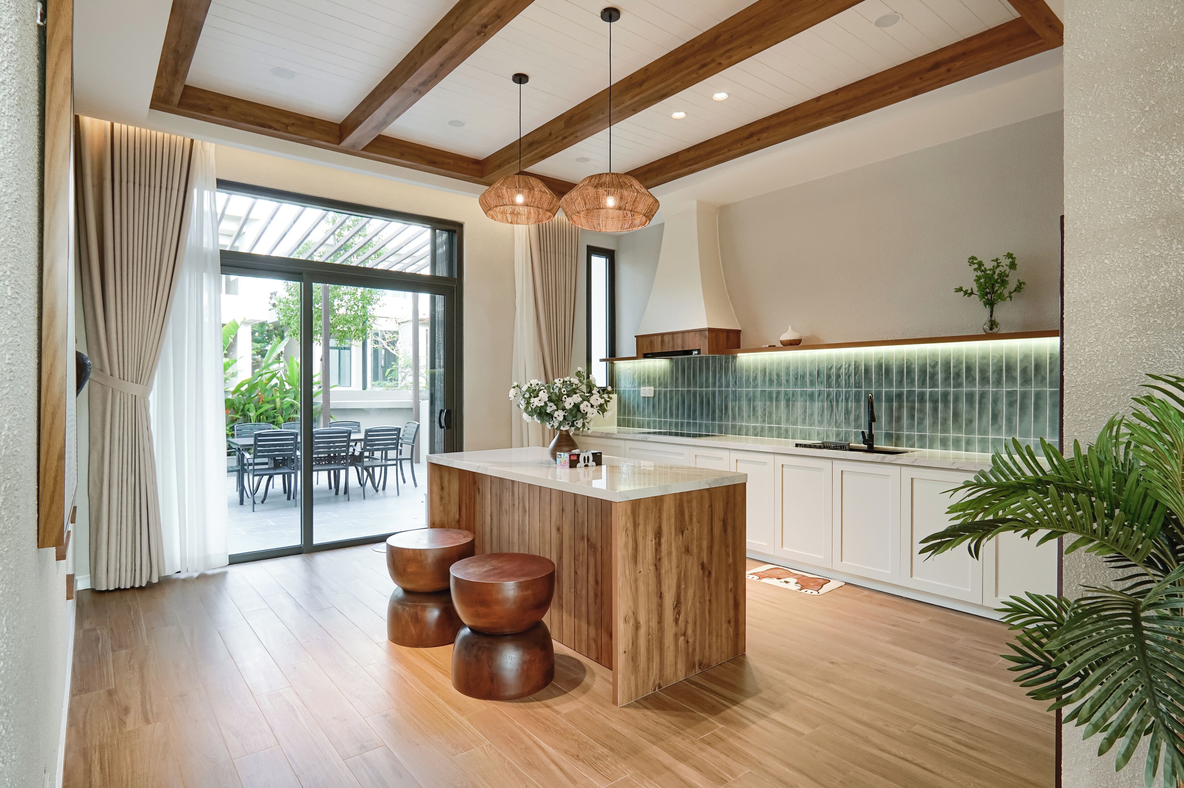 A modern kitchen with a wooden island, pendant lighting, and a view to the outdoor dining area.