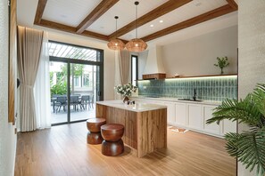 A modern kitchen with a wooden island, pendant lighting, and a view to the outdoor dining area. - Life Travel Villa - Novaworld Phan Thiet (Tien Thanh)