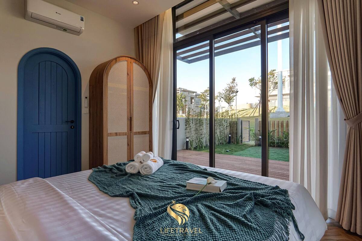 A bedroom with a bed, a blue door, a large window, and a view of a garden.