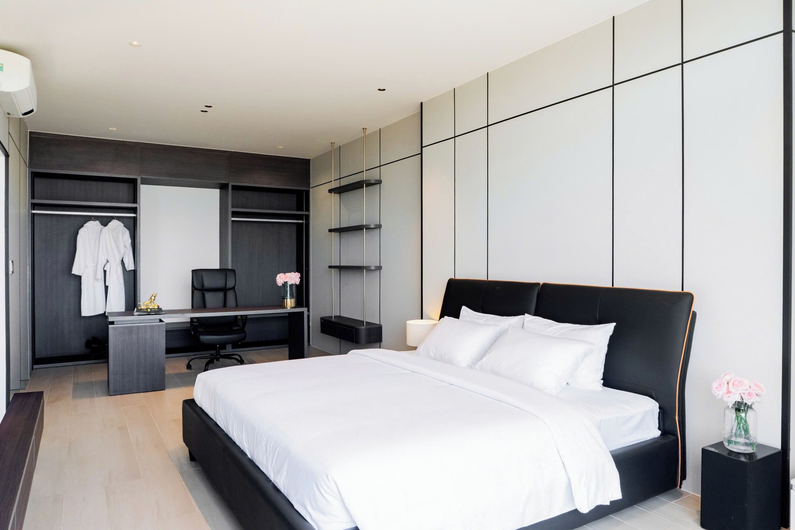 A modern bedroom with a large bed, a desk, a chair, a wardrobe, and a mirror.