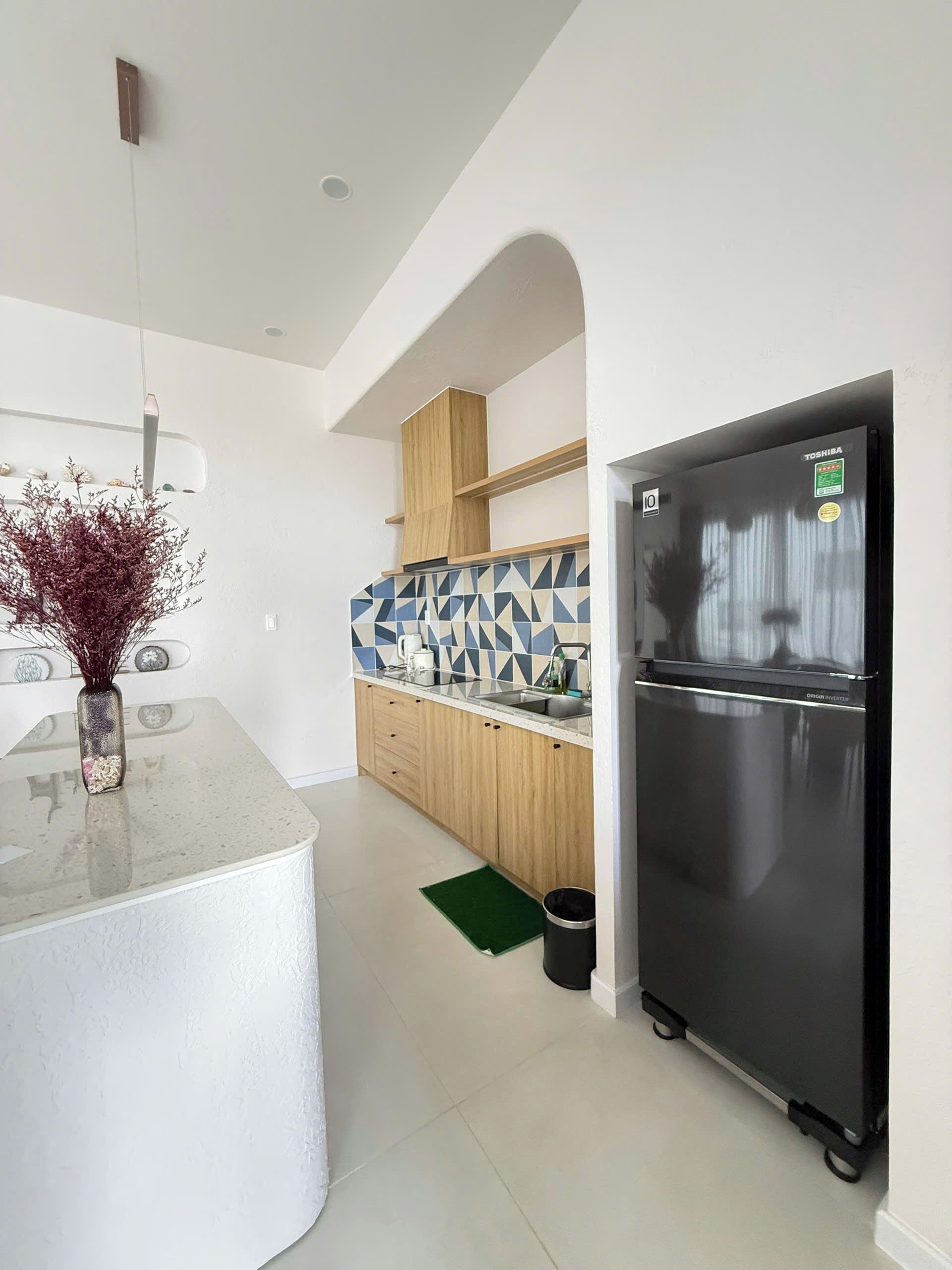 A kitchen with a black refrigerator, wooden cabinets, a white countertop, and a geometric backsplash.