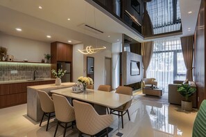 A modern kitchen with a central island, dining area with chairs, and a living space with a sofa and a TV. - Life Travel Villa - Novaworld Phan Thiet (Tien Thanh)
