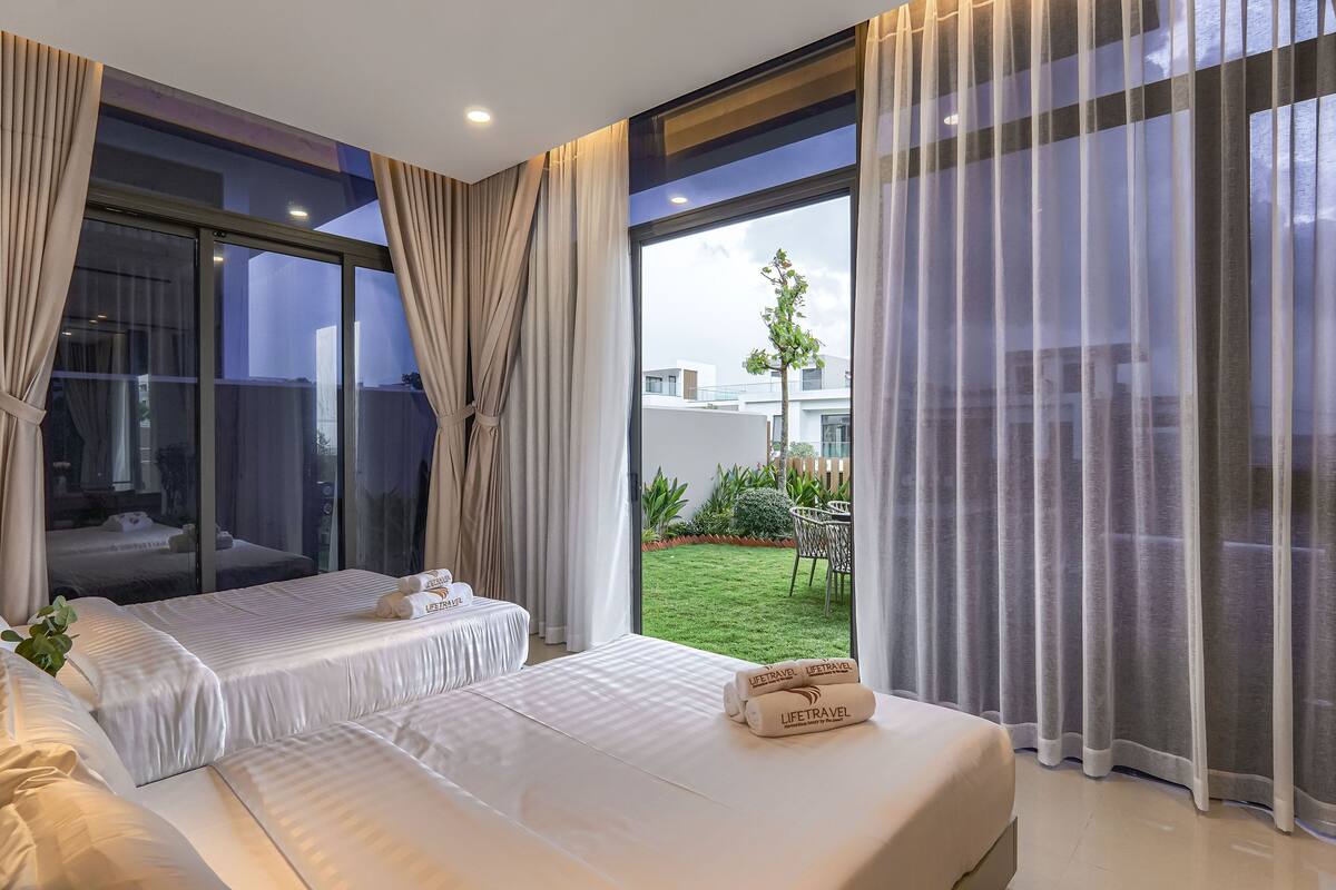 A modern hotel room with a large sliding glass door to a balcony, a bed with white linens, and a small table with a plant.