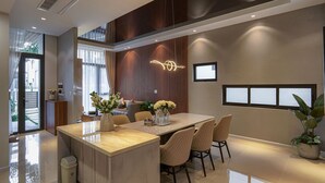 A modern dining area with a central island, cushioned chairs, and a contemporary light fixture. - Life Travel Villa - Novaworld Phan Thiet (Tien Thanh)