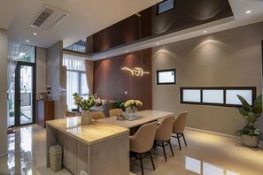 A modern dining area with a central island, cushioned chairs, and a contemporary light fixture. - Life Travel Villa - Novaworld Phan Thiet (Tien Thanh)