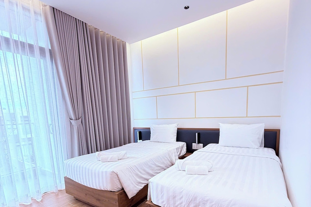 A hotel room with two beds, a large window with curtains, and a modern wall design.