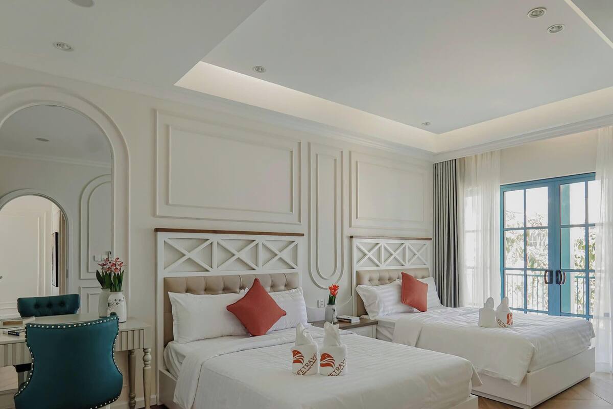A hotel room with two beds, a desk, a chair, and a large window.