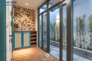 A modern interior with a stone wall, wooden flooring, and a view of bamboo plants outside. - Life Travel Villa - Novaworld Phan Thiet (Tien Thanh)