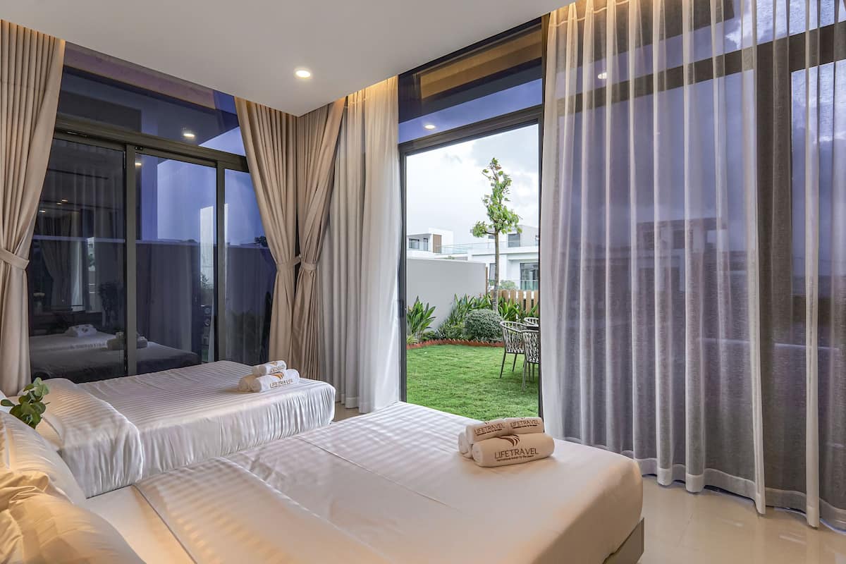A modern hotel room with a large sliding glass door to a balcony, a bed with white linens, and a small table with a plant.