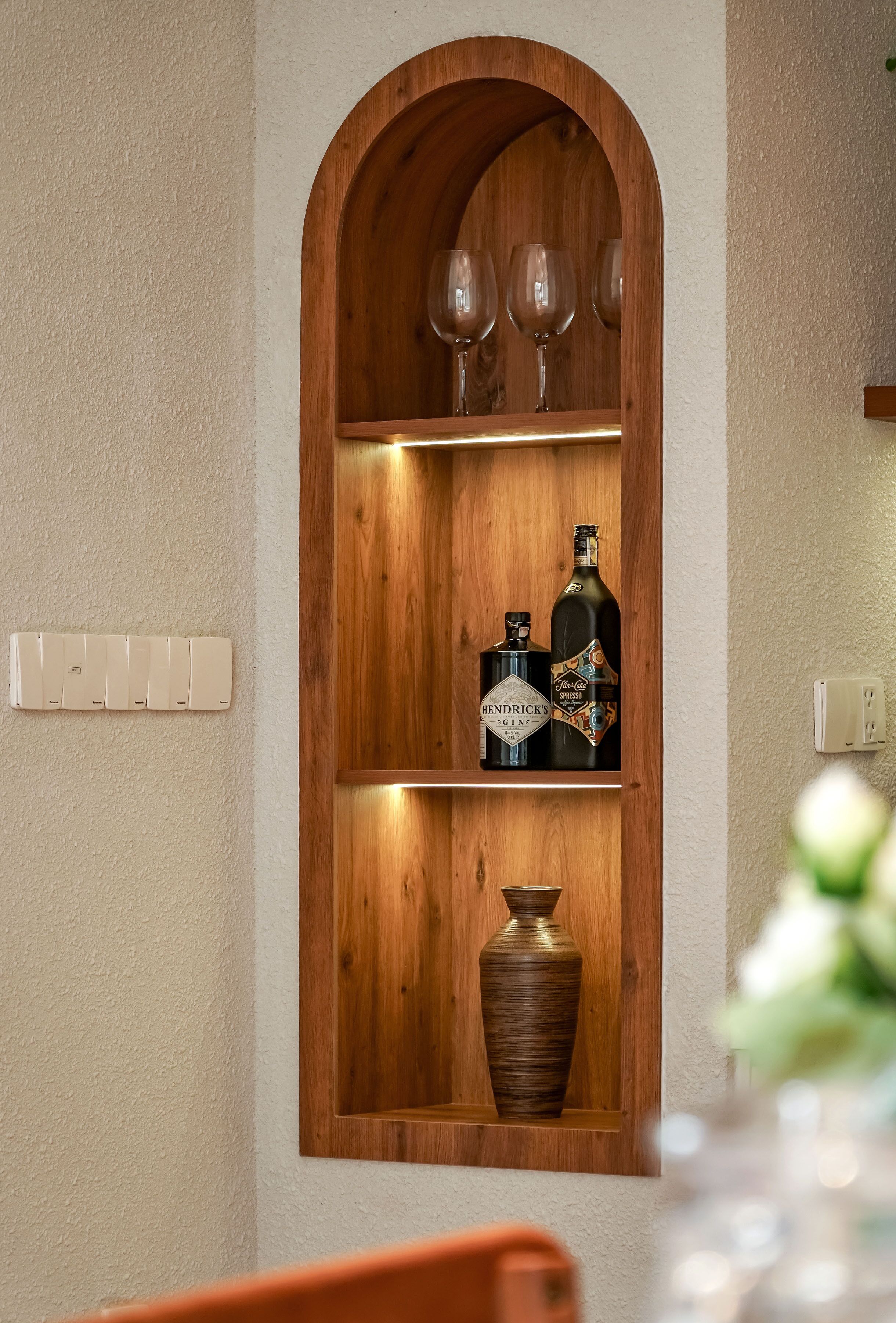 A wooden shelf with wine glasses, a bottle of Hendrick's Gin, and a vase.