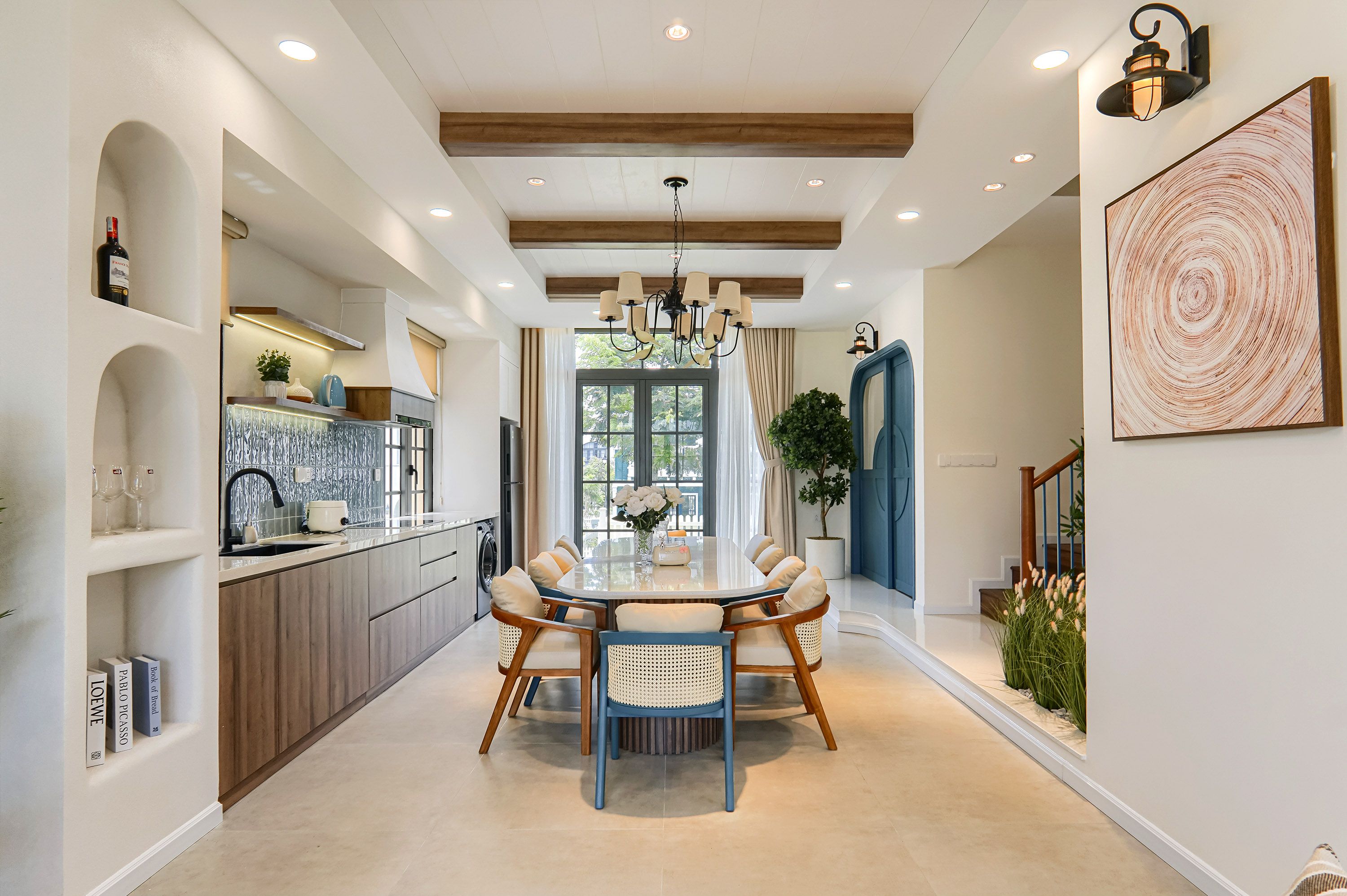 A modern kitchen with a dining area, featuring a round table with chairs, a chandelier, and a large window.