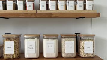 Two wooden shelves with glass jars labeled with various food items like pasta, flour, and rice.